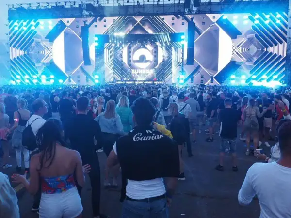 Tłum ludzi na festiwalu Sunrise w Kołobrzegu, podziwiający ogromną scenę z efektami świetlnymi.