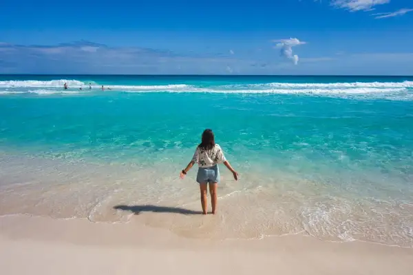 Frau steht im türkisfarbenen Meer, genießt das warme Wetter im Mexiko im Oktober. Der Strand ist sandig, das Wasser klar.