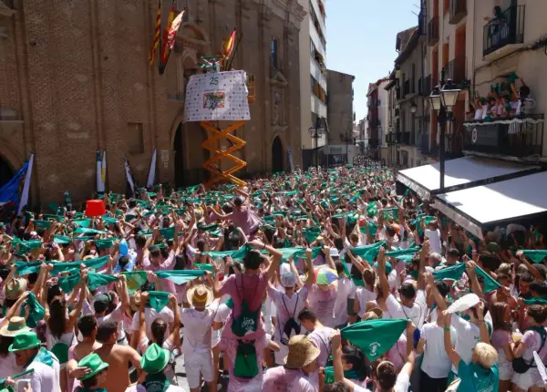 Multitud celebra el programa fiestas Huesca, agitando pañuelos verdes. Un cartel anuncia "25".