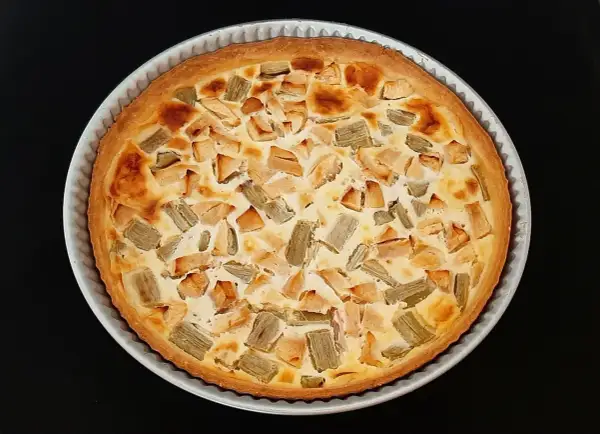 Tarte rhubarbe pomme dorée, garnie de morceaux de fruits et d'une crème onctueuse, prête à être dégustée.