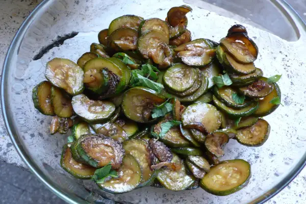 Zucchine alla scapece, fritte e condite con aceto e menta, in una ciotola di vetro.