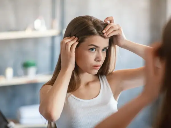 Junge Frau prüft im Spiegel ihre Haare und fragt sich, wie viel wachsen Haare im Monat.