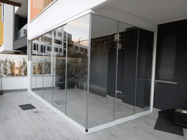 Veranda balcone con vetrate scorrevoli, luci decorative e piante. Spazio moderno e luminoso.
