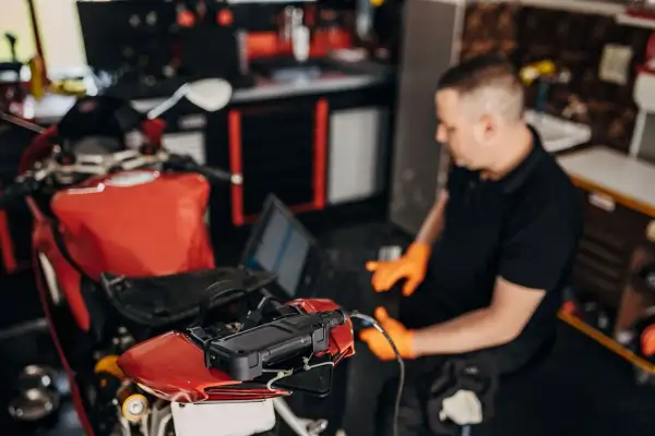 Mecánico con guantes naranjas usa un portátil para ver cómo se puede reprogramar una moto roja.