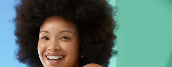 Rostro sonriente de mujer con afro, piel radiante. Evita la glicerina, es mala para la piel.
