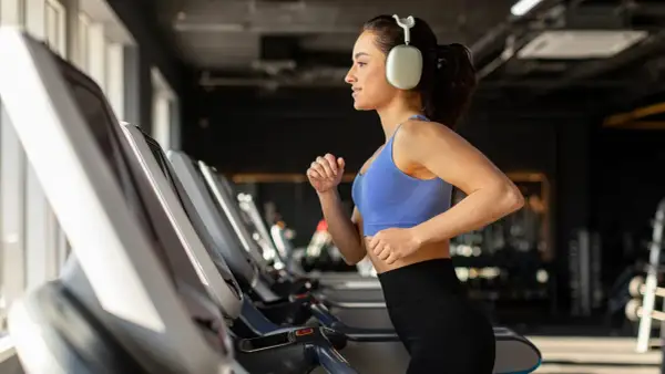 Junge Frau läuft auf Laufband im Fitnessstudio, motiviert für Fitness und Abnehmen.