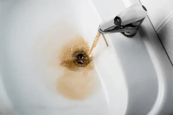 Acqua gialla dalla caldaia che scorre nel lavandino, creando un alone marrone.