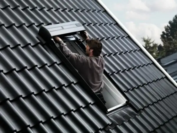 Un couvreur installe un volet roulant sur un toit en tuiles noires, un modèle velux 3uc b01 eu.