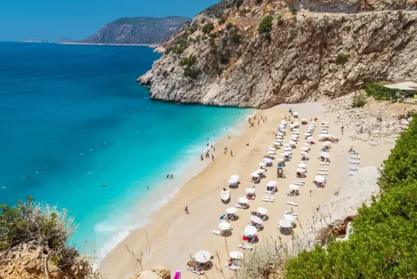 Malownicza plaża w Turcji z turkusową wodą i skalistymi klifami. Rzędy leżaków i parasoli zapraszają do odpoczynku.