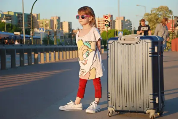 Dziewczynka z walizką czeka na wakacyjną przygodę. Może już niedługo przeczyta wierszyki o wakacjach krótkie, siedząc na plaży.