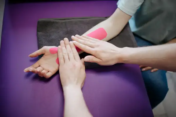 Fizjoterapeuta aplikuje taśmy kinezjotaping na nadgarstek pacjenta. Długość rehabilitacji po złamaniu nadgarstka zależy od wielu czynników.
