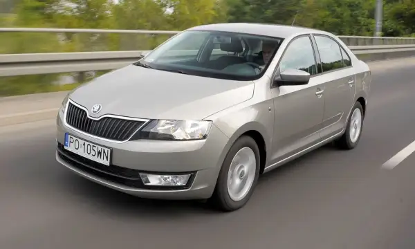 Srebrna Skoda Rapid jedzie po drodze. Kierowca jest widoczny za kierownicą. Wiele osób szuka skoda rapid opinie przed zakupem.