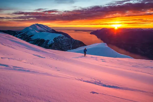 Alba infuocata sul lago di Garda in inverno. Un escursionista solitario cammina su un pendio innevato, godendosi la vista mozzafiato.