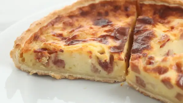 Un trozo de quiche de verduras con trocitos de bacon, horneado hasta dorarse.