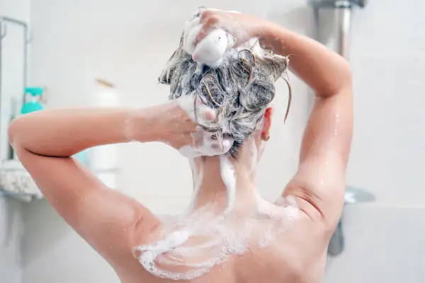 Persona lavándose el cabello con champú sin sulfatos, creando espuma abundante para una limpieza suave.