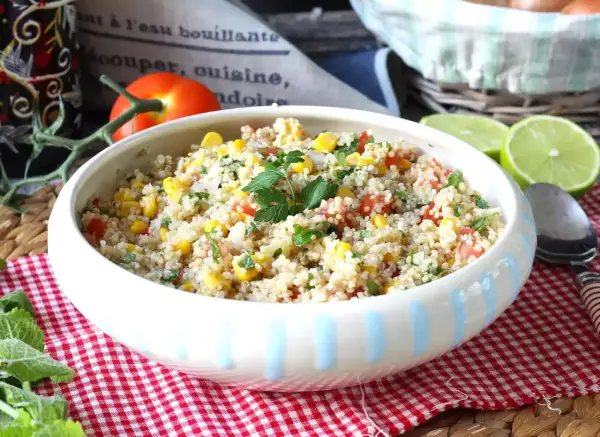 En skål med färgglad quinoa sallad med majs, tomat och persilja, garnerad med limeklyftor.