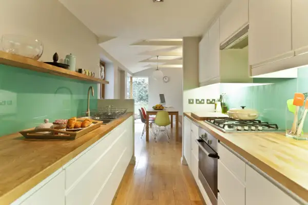 Cocina moderna con encimeras de madera, salpicadero verde menta y electrodomésticos integrados. Ideas para como diseñar una cocina funcional y estilosa.