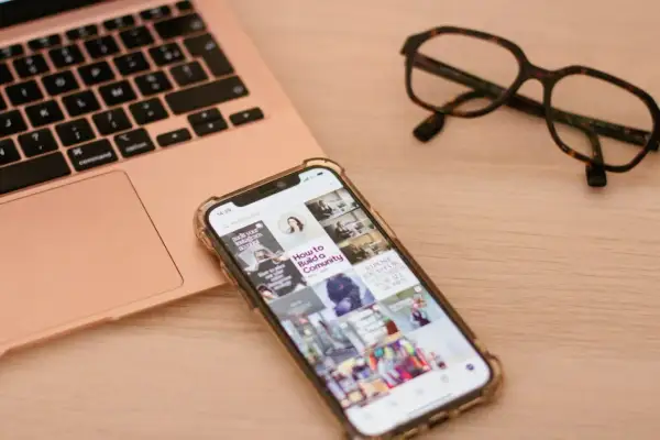 Telefon z uszkodzonym ekranem obok laptopa i okularów. Szukasz sposobu, jak wyświetlić uszkodzony ekran telefonu na komputerze?