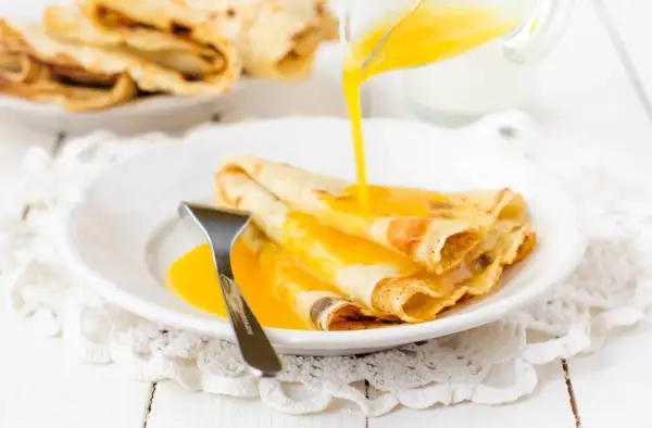 Złociste crepes suzette polane gorącym sosem, gotowe do zjedzenia.