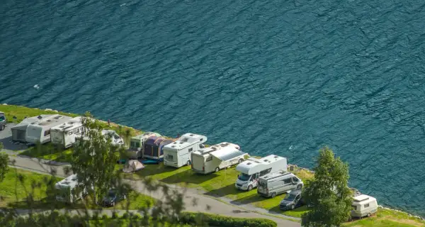 Un garaje al aire libre con varias caravanas y autocaravanas aparcadas junto a un lago azul.