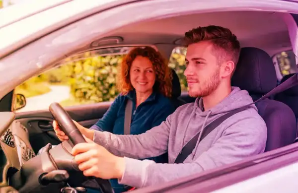 Giovane uomo guida, madre sorride. Ricorda che l'assicurazione auto deve essere intestata al proprietario per la massima tranquillità.