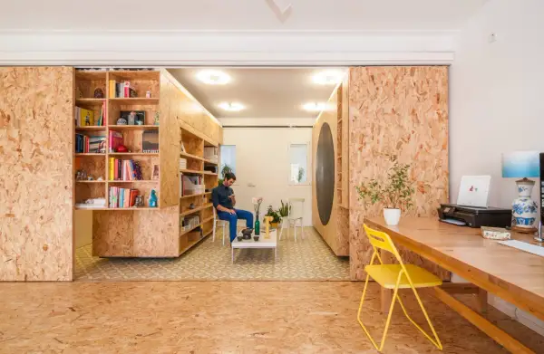Ein Mann sitzt in einem Raum, der mit OSB-Platten für den Innenausbau gestaltet ist. Bücherregale und ein Schreibtisch sind ebenfalls aus OSB gefertigt.