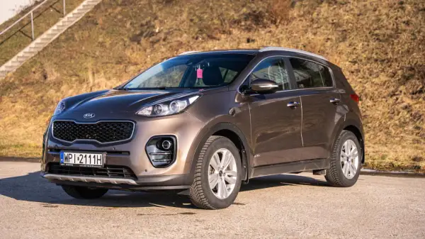 Brązowy Kia Sportage 2020 zaparkowany na drodze, z widocznymi schodami w tle.