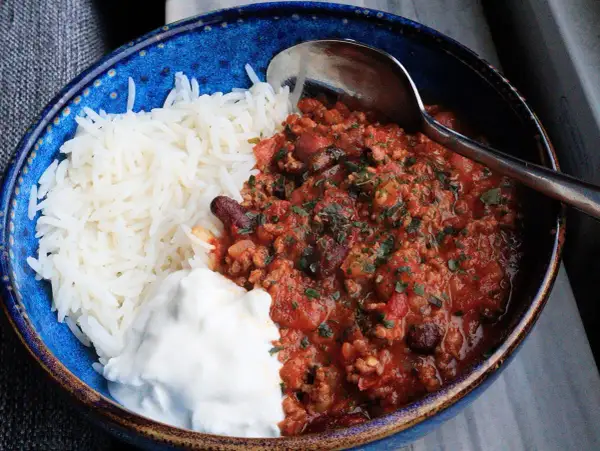 En blå skål med ris, en klick gräddfil och en portion av det godaste chili con carne, toppad med persilja.