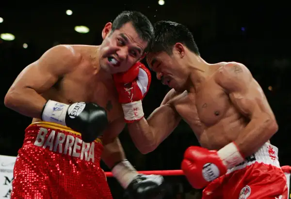 A boxer wearing red shorts with "BARRERA" emblazoned on them takes a hit.