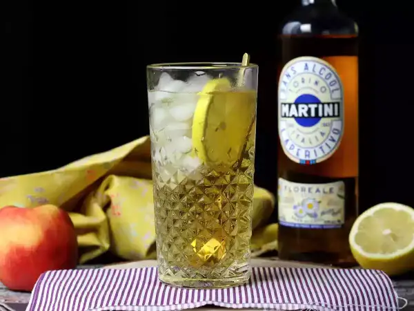 Orzeźwiający Martini Floreale z lodem i cytryną, obok jabłka i butelki Martini.