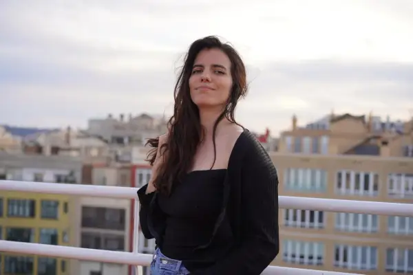 Anna Pazos, con su cabello suelto y una mirada serena, posa en una terraza con edificios de fondo.