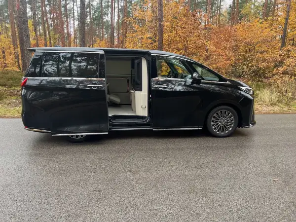 Lexus LM 350h w czarnym kolorze, z otwartymi drzwiami, prezentuje luksusowe wnętrze. Otoczony jesiennym lasem.