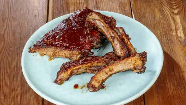 Succulente costine di maiale glassate con salsa barbecue, servite su un piatto azzurro su un tavolo di legno.