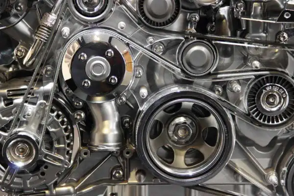 Détail d'un moteur chromé, avec la courroie de distribution tendue entre plusieurs poulies.