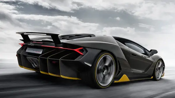 Czarny Lamborghini Centenario z żółtymi akcentami pędzi po drodze, chmury na niebie podkreślają dynamikę.