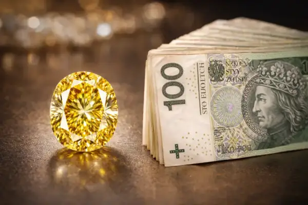 Olśniewający, duży, żółty diament lśni obok stosu banknotów 100-złotowych.