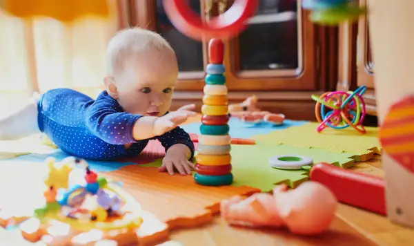 Dziecko bawi się kolorowymi, potencjalnie niebezpiecznymi zabawkami dla dzieci, takimi jak wieża z kółek i spiralna kula.