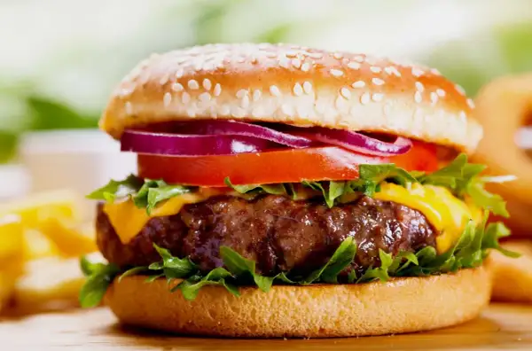 Soczysty burger z serem, pomidorem, czerwoną cebulą i sałatą na bułce z sezamem.
