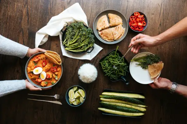 Stół z daniami: curry z kurczakiem, ryżem, brokułami, fasolką szparagową, ogórkami, limonkami i plackami.