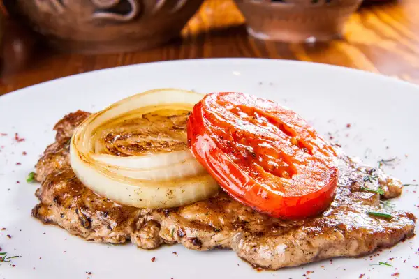 Karkówka pieczona w plastrach z cebulą i pomidorem. Aromatyczne danie, które zachwyci każdego smakosza.