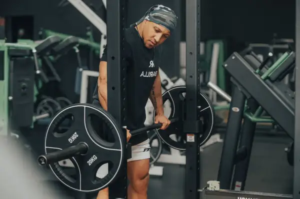 Mann mit Bandana macht schwere myo reps mit Langhantel im Fitnessstudio.