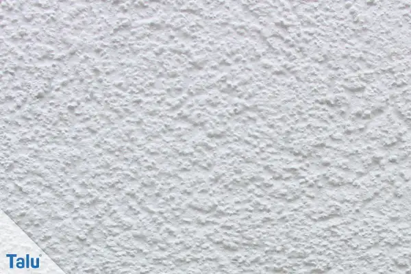 Nahaufnahme einer weißen, strukturierten Wand, die zeigt, wie man eine Wand verputzt. Das Korn ist unregelmäßig und erzeugt eine interessante Textur.