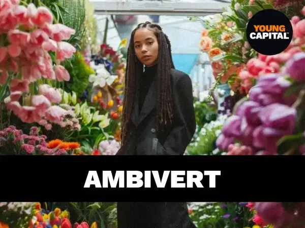 Een jonge vrouw met vlechten staat tussen bloemen. De tekst "AMBivert" suggereert de betekenis van ambivert: iemand die zowel extravert als introvert is.