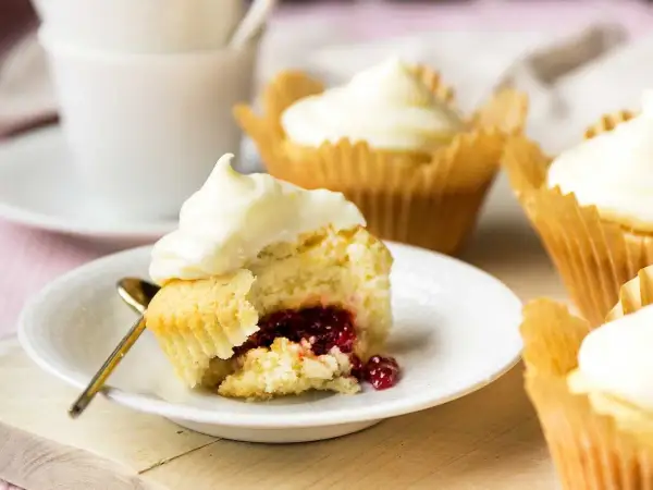 En närbild på en cupcake med vit frosting och en härlig röd fyllning. Flera liknande cupcakes med fyllning syns i bakgrunden.