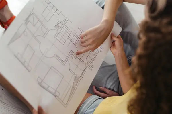 Dwie osoby analizują plan architektoniczny, omawiając, co to jest kondygnacja w budynku. Widoczne schody i pomieszczenia.