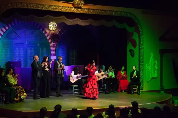 Una bailarina de **tango flamenco** con un vestido rojo y lunares negros cautiva en el escenario, acompañada por guitarristas y cantantes.