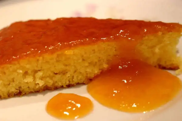 Una fetta di torta senza glutine, soffice e dorata, coperta da una lucida glassa all'arancia.