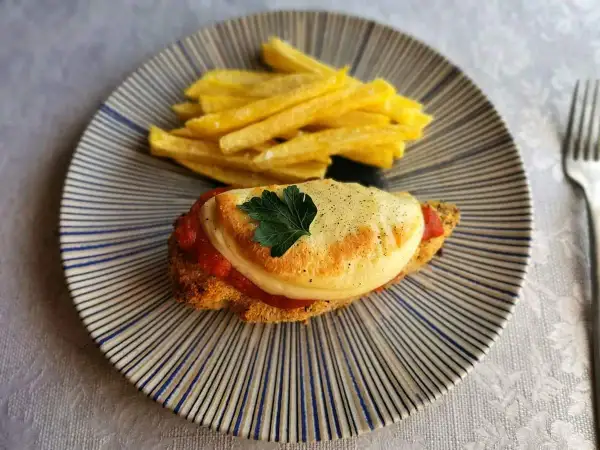 Delicioso pollo a la parmesana con papas fritas crujientes, servido en un plato rayado.