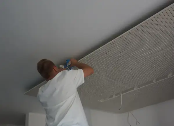 Mężczyzna montuje płyty karton gips na suficie w nieogrzewanym domu.