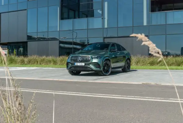 Zielony Mercedes-Benz GLE 450d coupe zaparkowany przed nowoczesnym budynkiem z lustrzanymi oknami.
